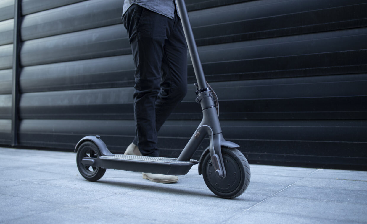 Unrecognizable modern person walking by his electric scooter.