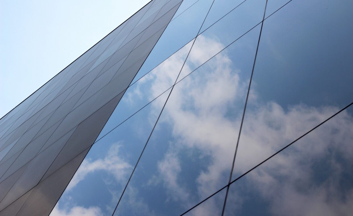 Low angle shot of a glass high-rise business building with a reflection of clouds and the sky on it