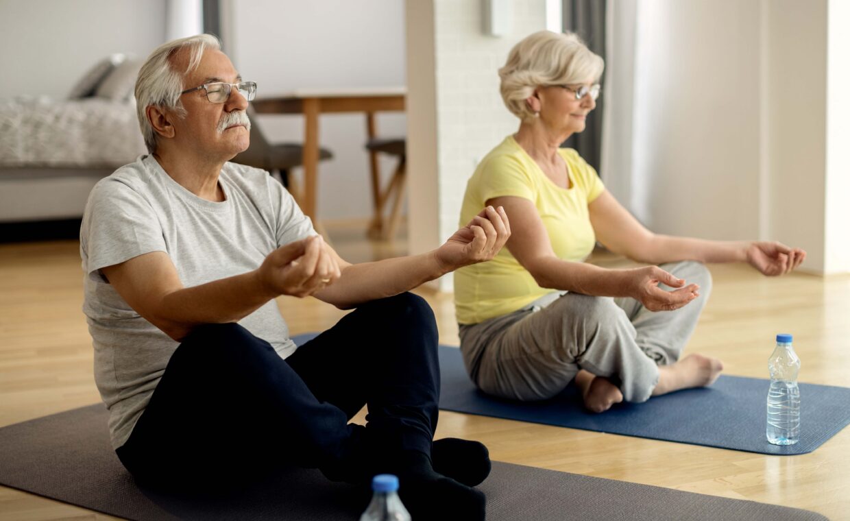 Mature couple meditating in lotus positing at home.