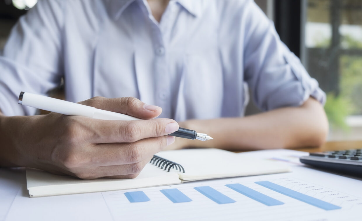 persona che scrive con grafici, calcolatrice e quaderno appunti