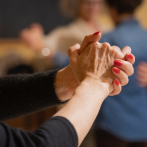 mani donna in primo piano in gesto di danza con coppia che balla sullo sfondo