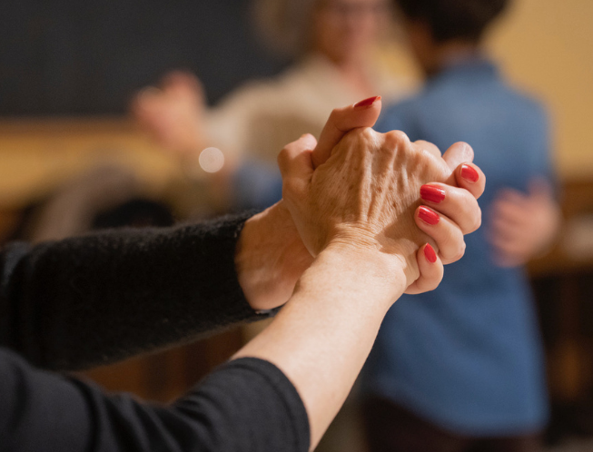 mani donna in primo piano in gesto di danza con coppia che balla sullo sfondo